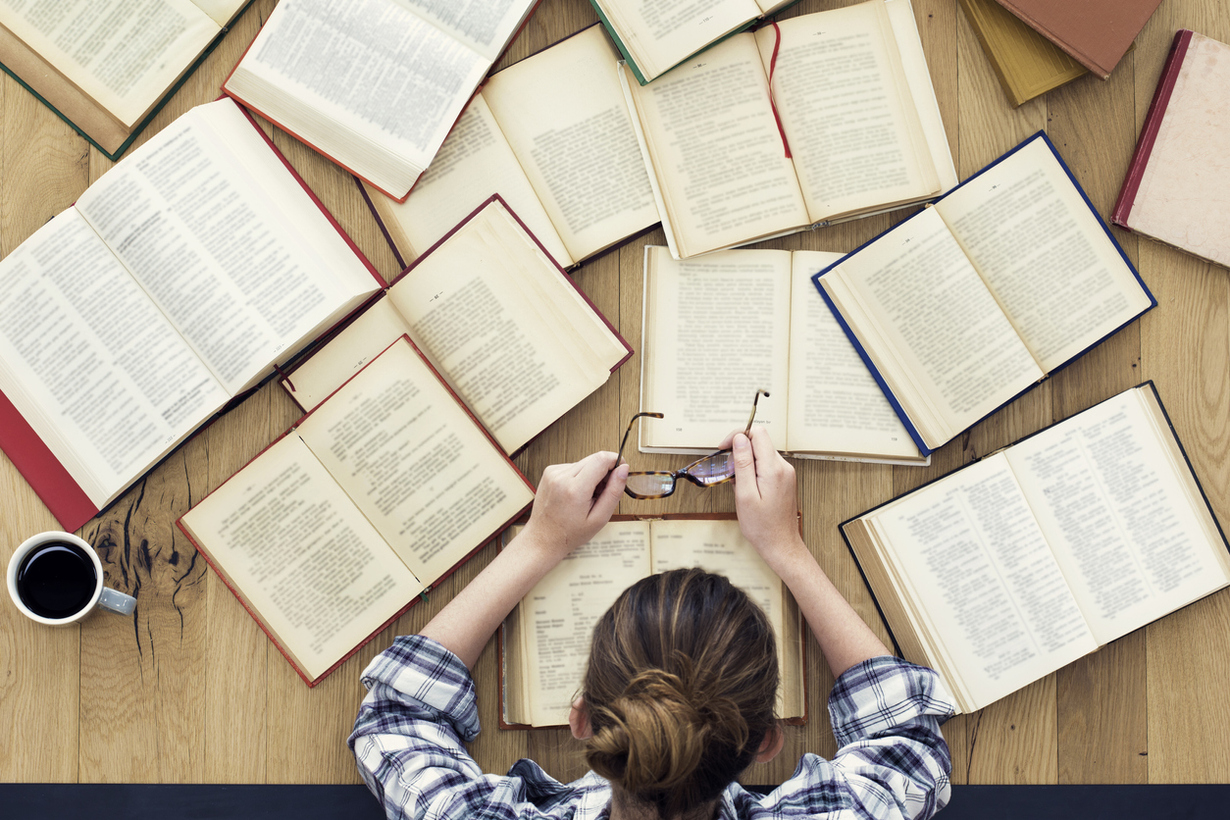 Key Visual des LernLABOR: Eine Frau liest zahlreiche Büchern, die aufgeschlagen auf einem Tisch liegen.